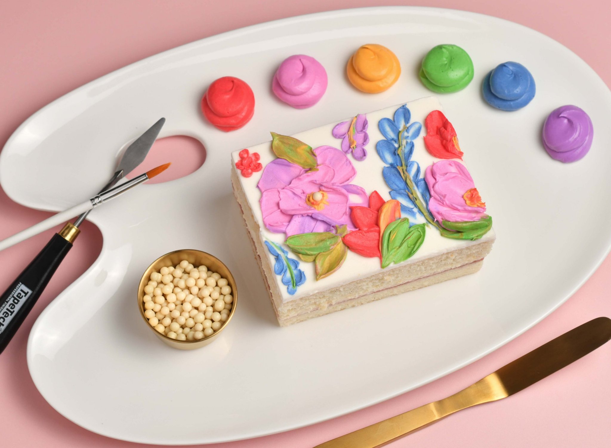 Ceramic plate with cake slice, assorted color buttercream and artist tools for Cakeistry event.